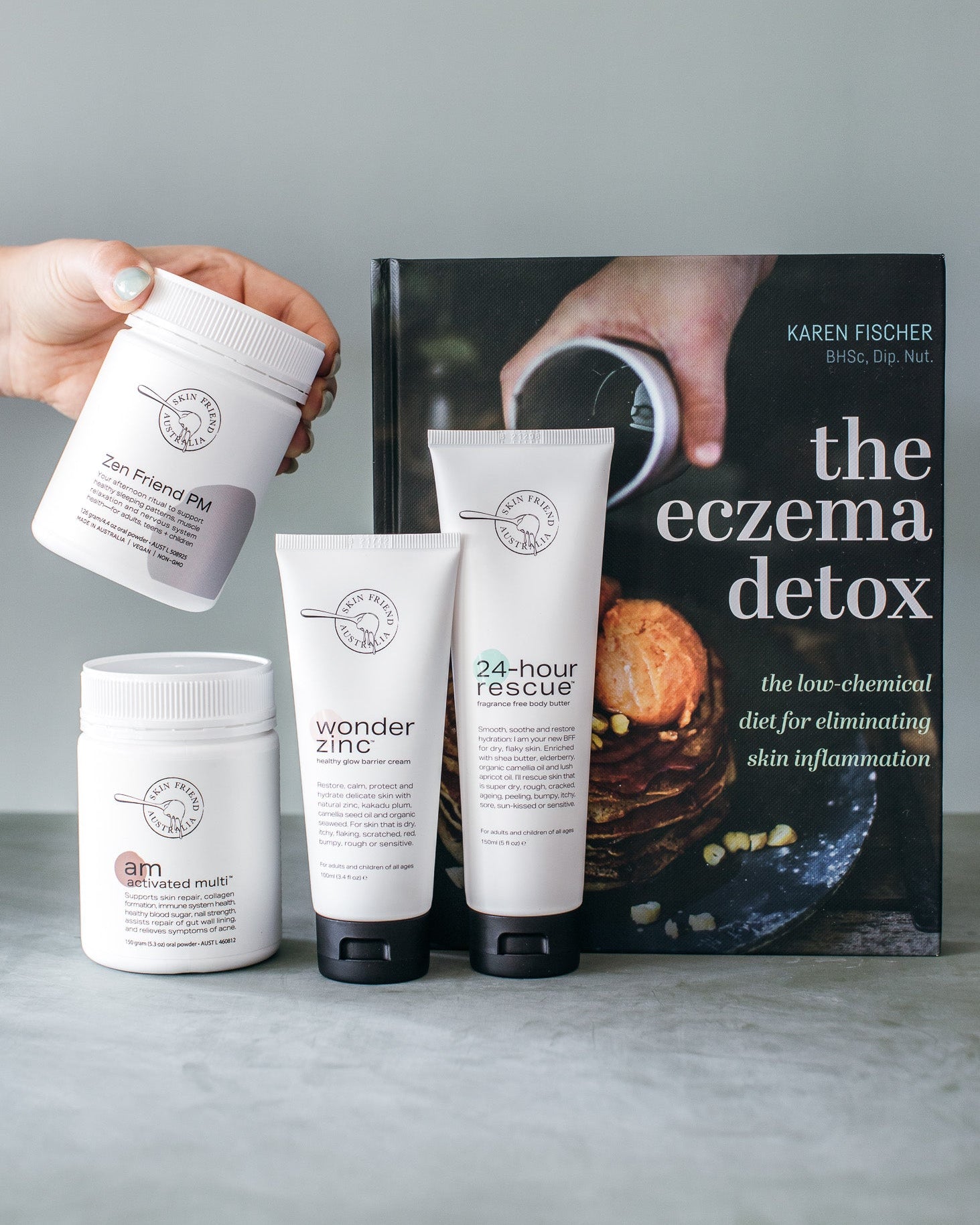 Skincare products and a book titled 'The Eczema Detox' on a gray surface.