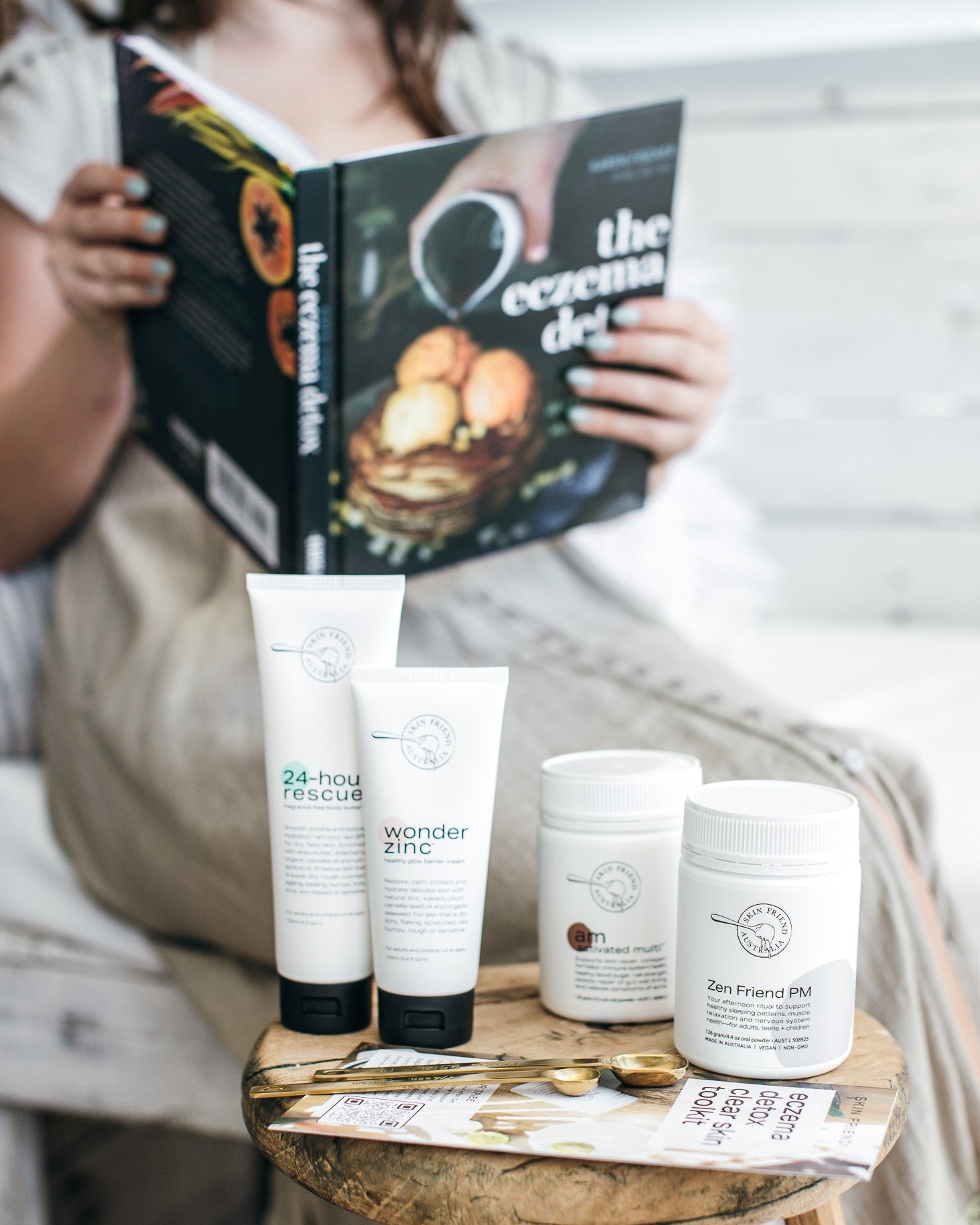Person reading a book with skincare products on a stool in the foreground
