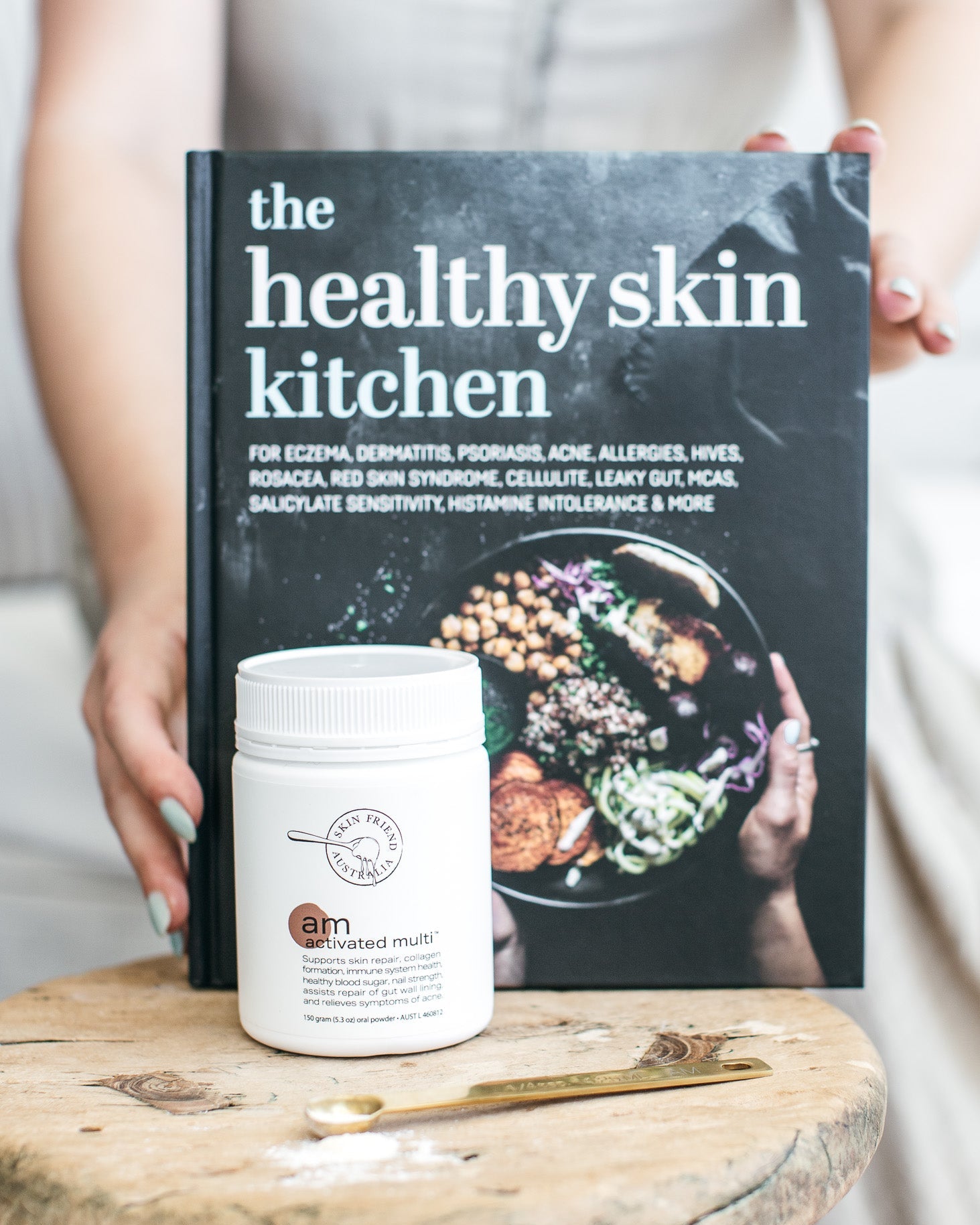 Book titled 'The Healthy Skin Kitchen' on a wooden stool with a container of 'tam' multivitamins.