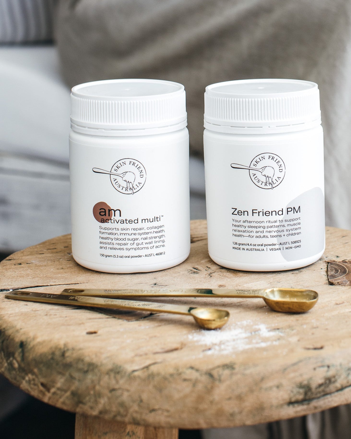 Two white containers labeled 'activated multi' and 'Zen Friend PM' on a wooden surface with gold spoons.