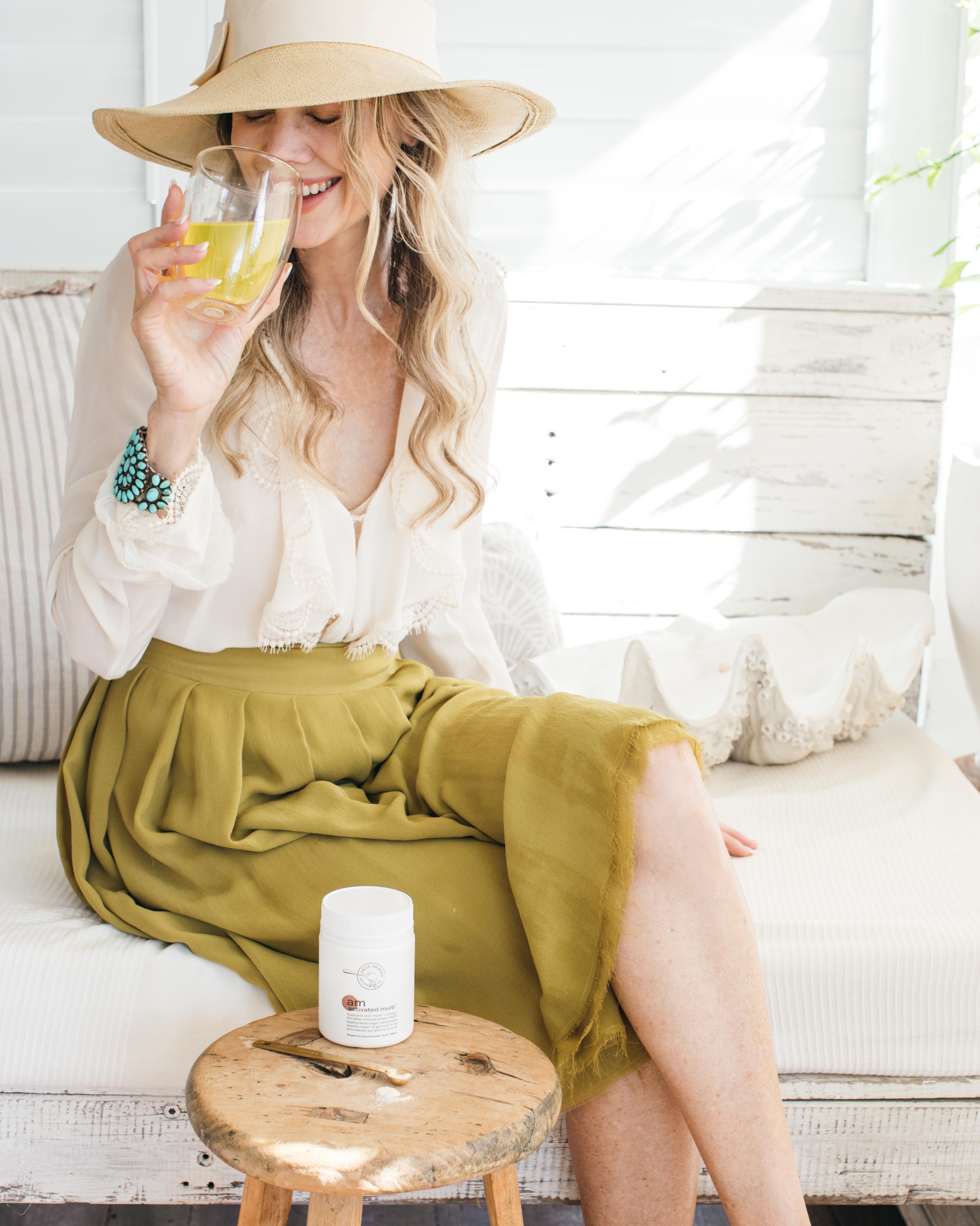 Woman in a white blouse and green skirt sitting on a white bench, holding a glass of orange juice.