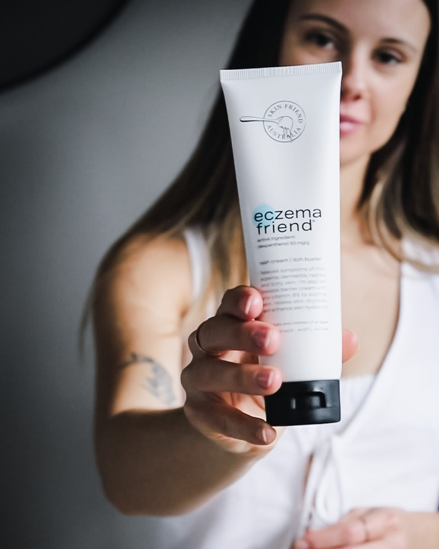 Person holding a tube of 'eczema friend' cream against a neutral background