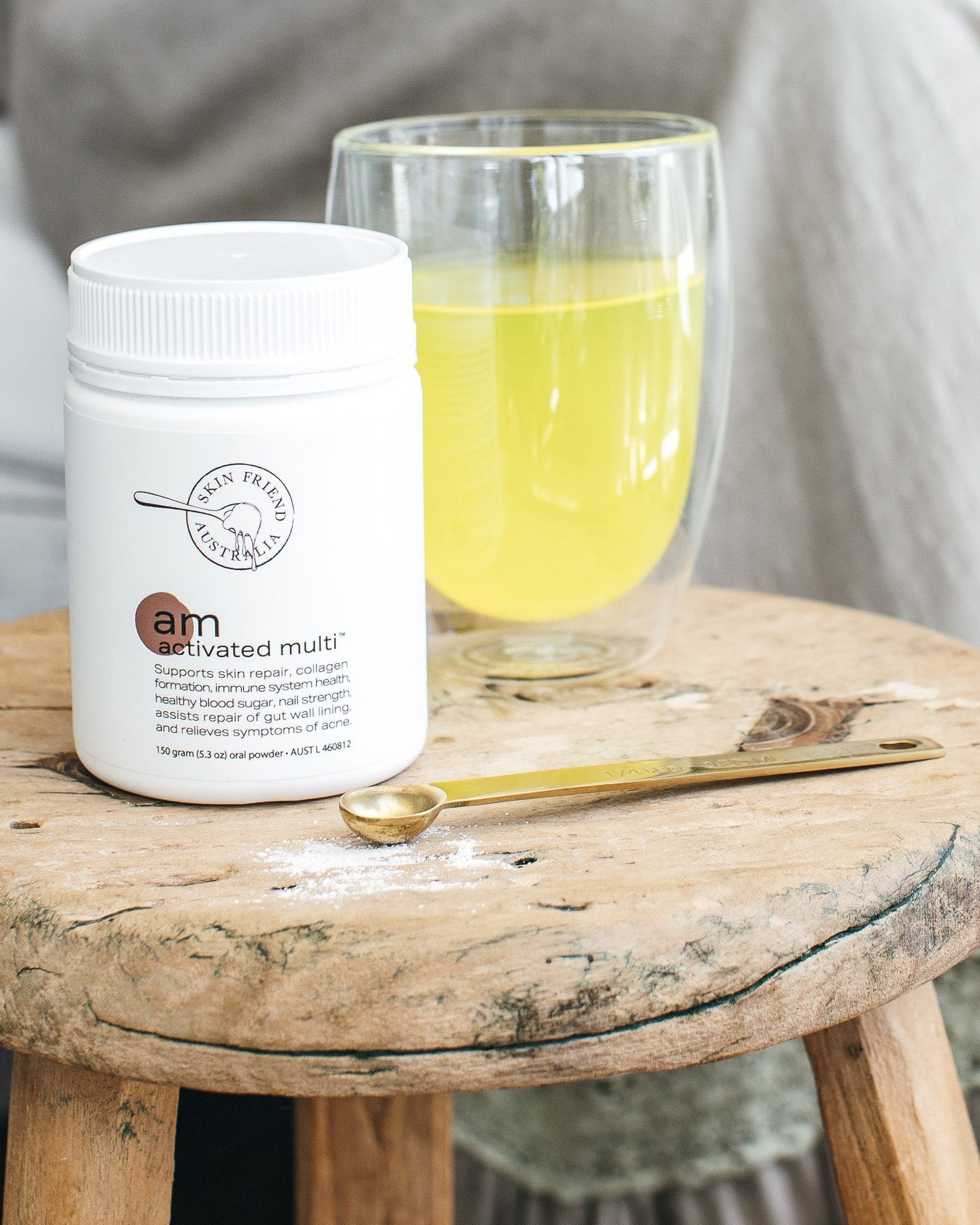 White container labeled 'Skin Friend AM' on a wooden stool with a glass of yellow vitamin liquid.